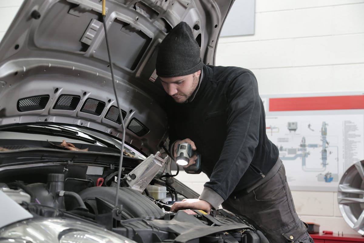 Kfz-Techniker beleuchtet den Motorraum bei der technischen Inspektion eines Pkw in der Werkstatt