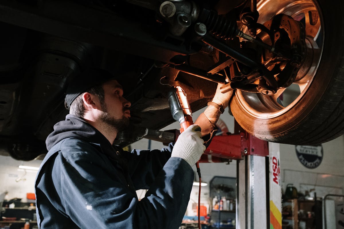 Mechaniker inspiziert die Fahrzeugunterseite an der Hebebühne mit Arbeitsleuchte – Fahrzeugreparatur in der Autowerkstatt